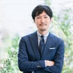 腕を組んでほほ笑むスーツの男性