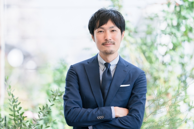 腕を組んでほほ笑むスーツの男性